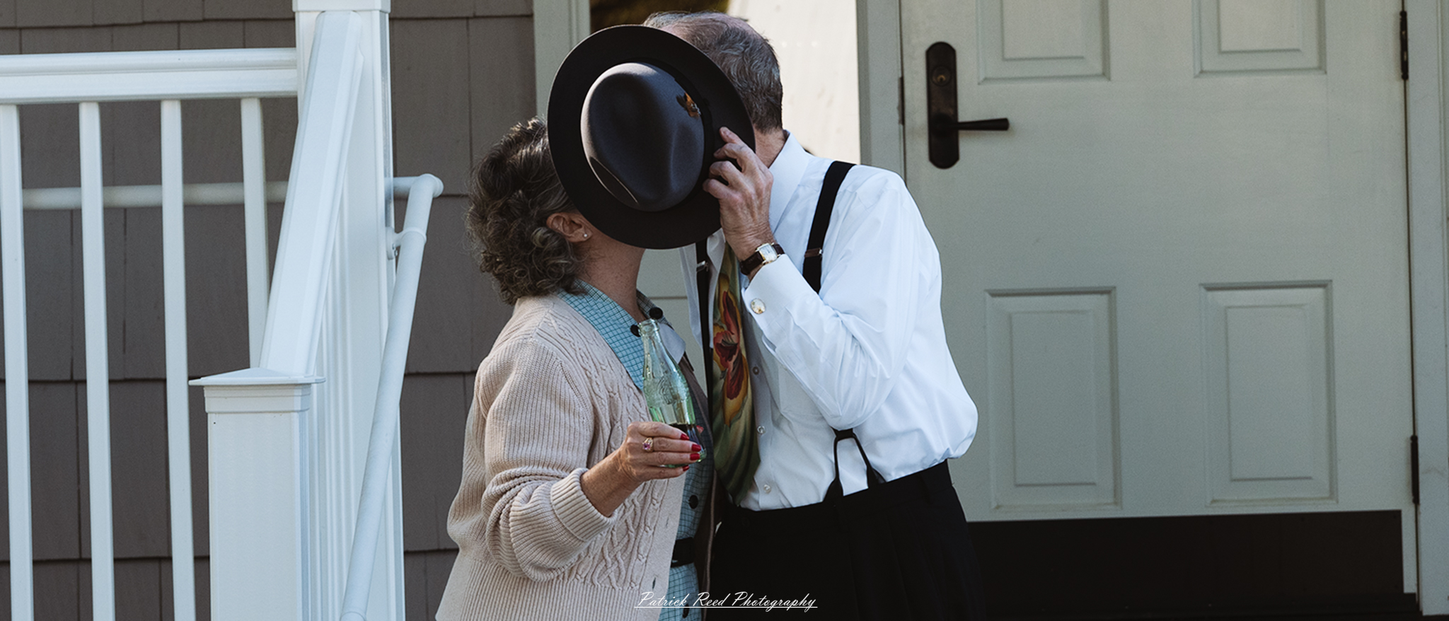 "A couple kissing in 1940s clothing, their faces hidden by the brim of the man's fedora. The man is dressed in a classic suit and the woman wears a vintage dress, evoking the style and charm of the World War II era. The intimate moment, framed by the fedora, adds a timeless and romantic feel to the scene, capturing a sense of nostalgia and love."